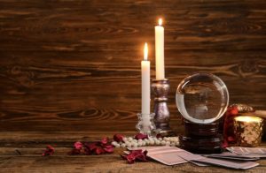 two burning candles with a crystal ball and cards in front